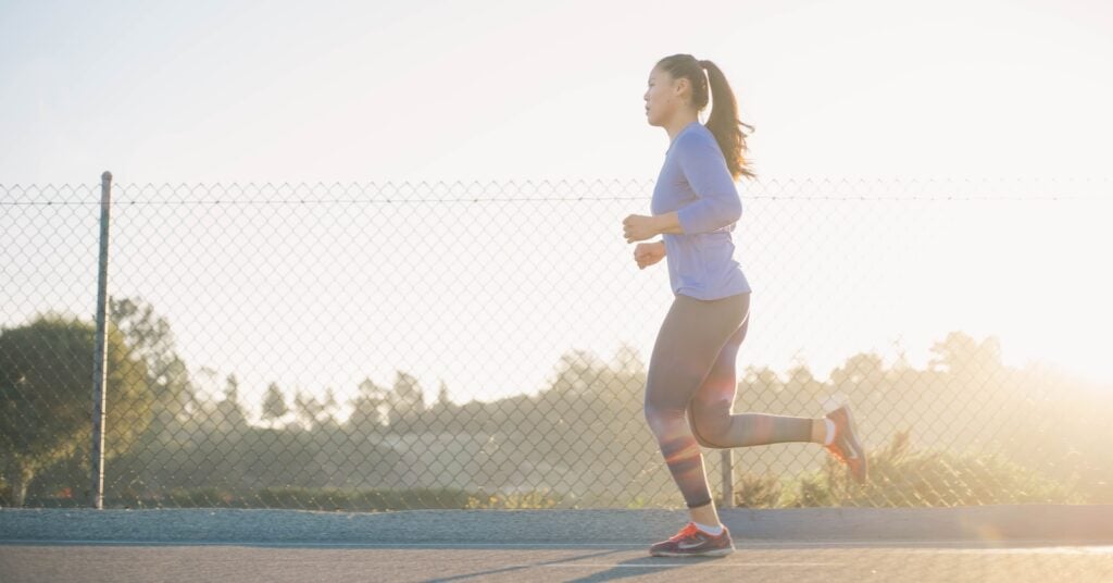 Woman jogging near a wire fence, symbolizing the journey to improved running endurance.