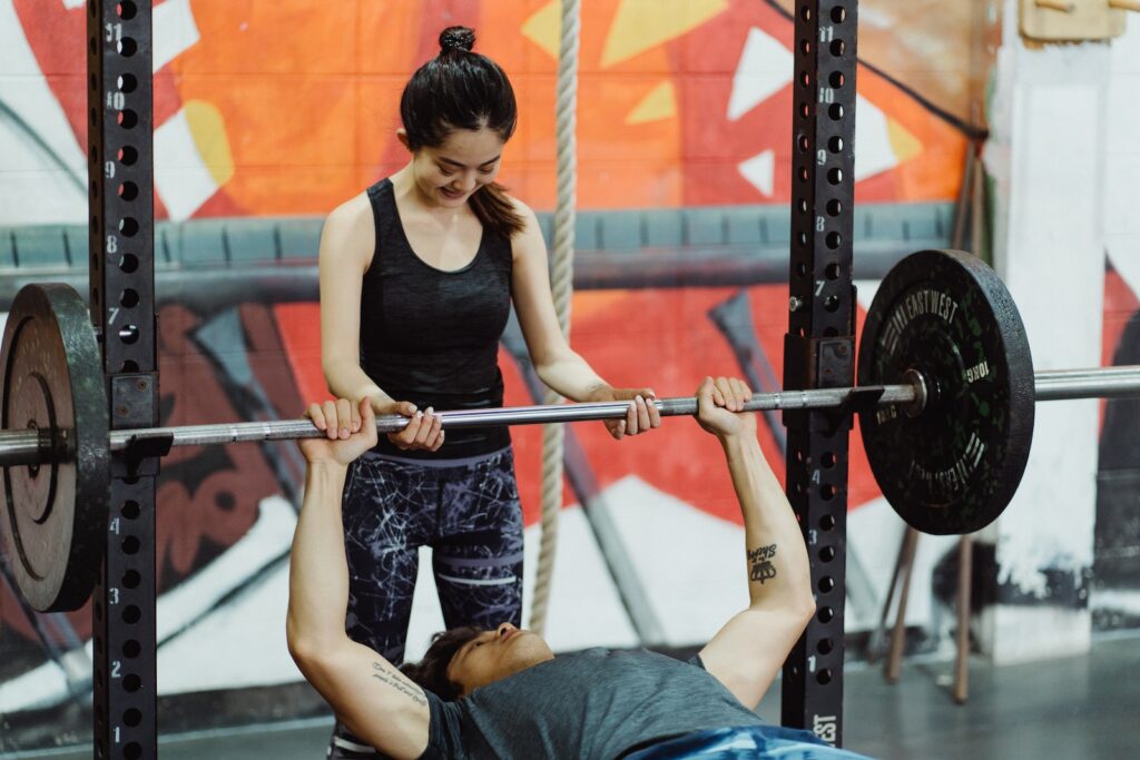 Man receiving assistance while doing bench press in a gym