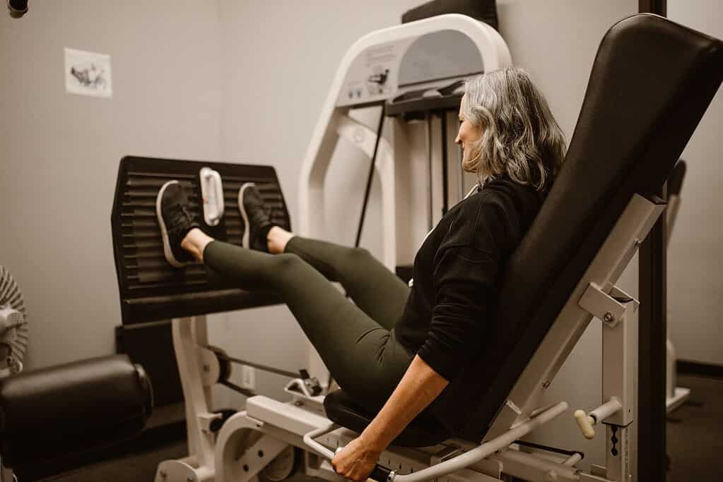 Woman performing leg press with legs fully extended but knees not locked.