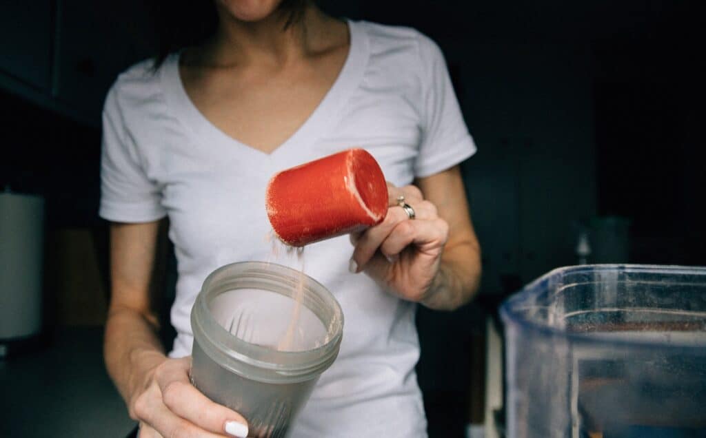 A person blending a protein shake with fruits and whey protein in a kitchen blender.