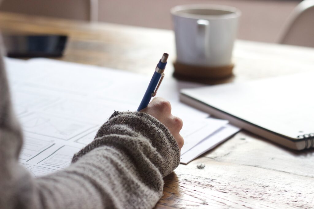 Individual jotting down notes at a table, illustrating the act of planning a fitness routine around a busy schedule.